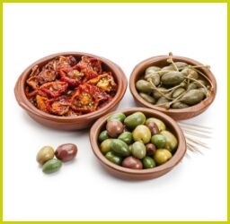 Feinkost-Auswahl mit grünen und schwarzen Oliven, getrockneten Tomaten und Kapern in Tonschalen auf weißem Hintergrund