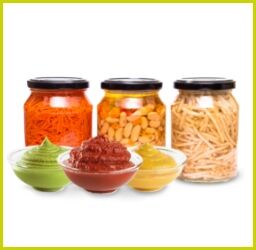 Drei Gläser mit eingelegtem Gemüse und Schalen mit grüner Paste, rotem Dip und Senf auf weißem Hintergrund